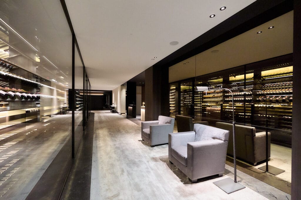 Naadloos spanplafond met geïntegreerde verlichting in een luxe wijnkelder met glazen wijnwanden en zithoek.
