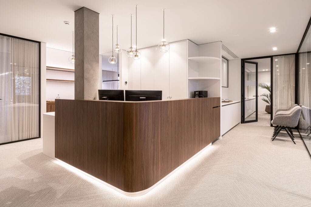 Moderne ontvangstbalie in een gerenoveerd architectenbureau met witte akoestische spanplafonds, houten balie en glazen vergaderruimtes.