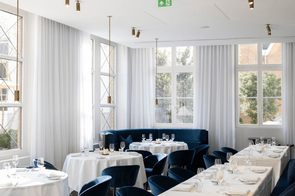Restaurantinterieur van Bar Bulot in Botanic Sanctuary Antwerp met witte akoestische spanplafonds, hoge ramen en blauwe zitbanken.